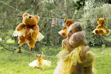 Girl in tutu cuddles teddy among hanging toys in garden.