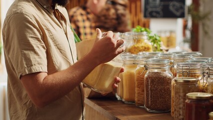 Man in zero waste supermarket thoroughly checking products before making purchase decision, making...