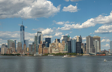 New York, NY, USA - August 1, 2023: Southern tip of Manhattan island under blue cloudscape. Green battery park in front of skyscraper collection in Financial District. One World Trade Center is talles