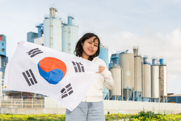 Positive young woman posing with South Korea flag in hands against background of factory