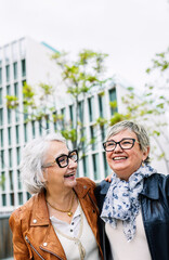 Two senior adult women having fun together at city street. Friendly female friends laughing while...