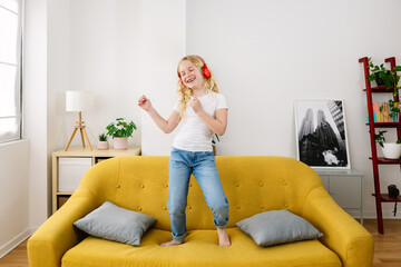 Little girl dancing on sofa while listening music. Joyful 7 years old kid having fun at home