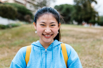 Young smiling student asian girl looking at camera standing at college campus. Education and people concept.
