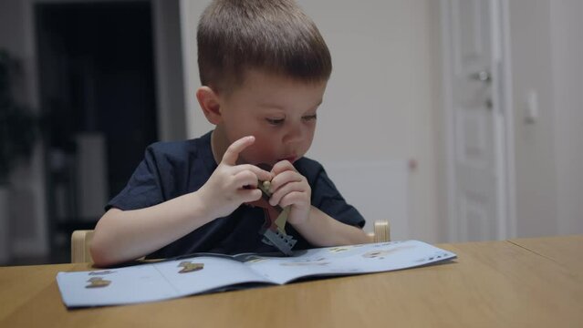 Sitting at table young child playing toy constructor following instructions. Child playing with blocks bricks and cubes construct new toy following instructions colorful world of toy constructor set