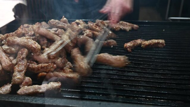Cevapcici or cevapi on the grill. Man grilling meat. Grilled dish of minced meats on the barbecue.  