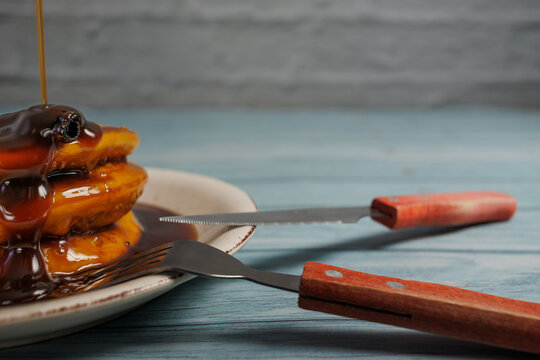 opaipillas pasadas, with a splash of chancaca syrup drizzled over them, on a light blue wooden table on a rustic white wall background. Typical Chilean food