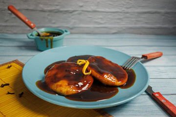 Sopaipillas, in a blue plate with an orange peel on top. Utensils, bowl with chancaca. Cloves scattered on the wooden table. Typical Chilean food