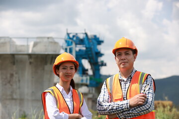 Senior construction male  engineer training a young new female  engineer and using a digital tablet with a hold walkie-talkie in his hand at the infrastructure of Sky bridge