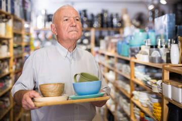 Elderly male customer chooses plates and cups in tableware store