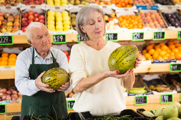 Grocery supermarket worker helping woman pick ripe watermelon