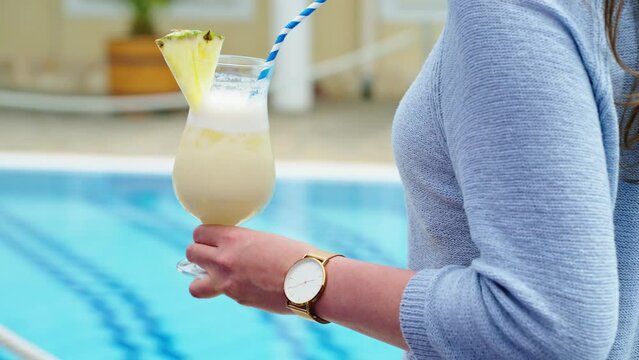 Woman drinking cocktail at poolside in summer. Relaxing vacation. Slow motion 4k video, copy space at end.