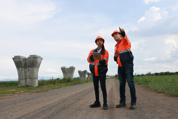 Senior construction male  engineer training a young new female  engineer and using a digital tablet with a hold walkie-talkie in his hand at the infrastructure of Sky bridge