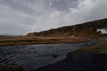 Stream in meadow with rainbow on cloudy day