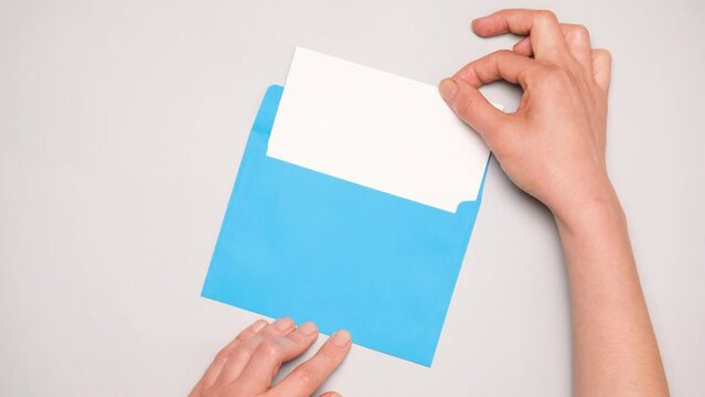 A hand pulls out a white card from a bright blue envelope. Top view of a blue envelope on gray background. Banner for social media ad with copy space.
