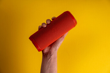Hand holding bluetooth loudspeaker on yellow background
