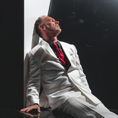  Distressed man in professional attire, slumped in defeat portrays a sense of overwhelming stress and defeat. High contrast lighting against a dark backdrop.