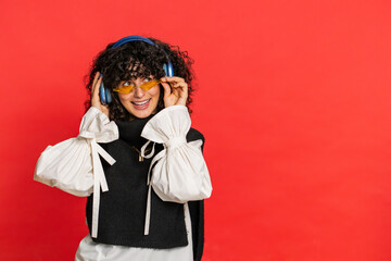 Caucasian young woman with curly hair listening music on headphones, dancing disco fooling around...