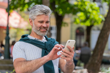 Happy smiling mature man using smartphone typing text messages tired looking up thinking and...