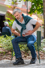 Obraz premium Caucasian mature man feeling sudden strong abdominal stomach ache, gastritis problem. Upset tourist guy having symptom poisoning diarrhea indigestion peptic ulcer pancreatitis on city urban street.