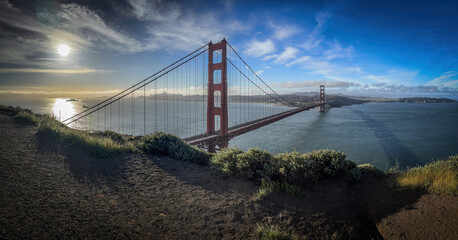 Panoramic view of Golden Gate Bridge and cityscape of San Francisco, California, USA at sunrise against blue sky with clouds