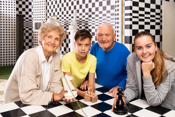 Grandparents with grandchildren are satisfied after visit of escape room stylized under chessboard