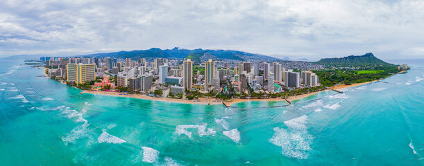 Aerial panoramic shot of Waikiki Beach in Honolulu under overcast skies with rain on the mountains - Powered by Adobe