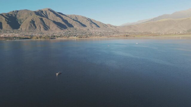 Aerial Tracking Fishermen In Fishing Boat. Over Water With Desert Mountain Landscape In The Distance. Beautiful Reflections On The Water. Dique la Angostura In Taf&iacute; del Valle, Tucum&aacute;n, Argentina