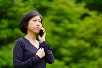 緑の中で泣きそうな顔で電話する中年女性