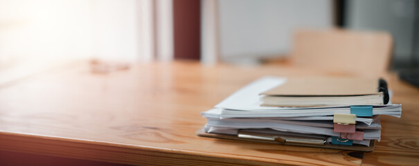 A stack of papers on a wooden table with a clip board on top