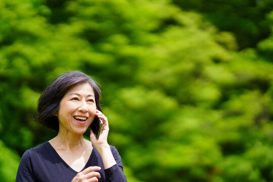 緑の中で笑顔で電話する中年女性