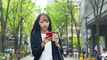 Fototapeta premium スマホを見ながら街を歩く女性ビジネスパーソン