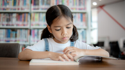 A young girl is sitting at a table in a library, reading a book