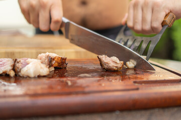 Man cutting meat on wooden cutting board during barbecue
