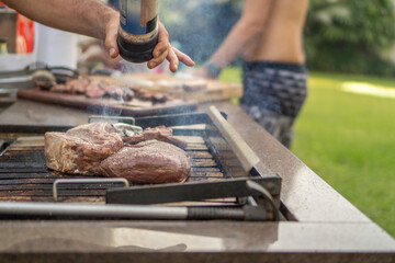 Man seasoning meat on a barbecue grill in the garden