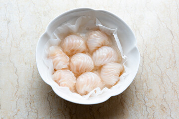 Dim sum for Chinese breakfast tea includes steamed shrimp dumplings served on a round plate with oiled paper.