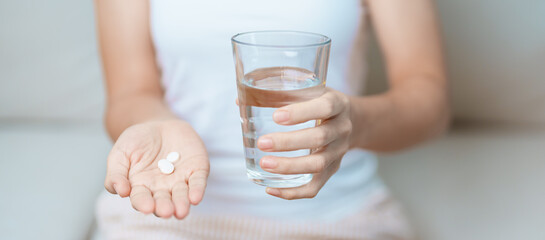 woman hand holding medicine painkiller pill and water glass on the sofa at home, taking for...