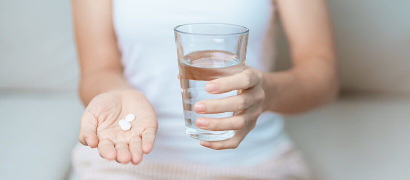 woman hand holding medicine painkiller pill and water glass on the sofa at home, taking for headaches, stomach ache, Diarrhea Pain from food poisoning, Endometriosis, Hysterectomy and Menstrual