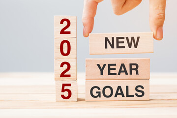 hand holding wooden block with text 2025 NEW YEAR NEW GOALS on table background. Resolution,...