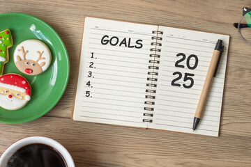 2025 GOAL with notebook, black coffee cup, Christmas cookies and pen on wood table. Xmas, Happy New...
