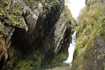 A waterfall sandwiched between two rocks, a stormy stream flows down an autumn forest on a cloudy day.