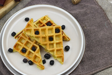 Waffle with dried blueberry topping and honey. Breakfast concept with grey background.