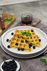 Waffle with dried blueberry topping and honey. Breakfast concept with grey background.