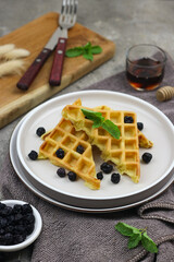 Waffle with dried blueberry topping and honey. Breakfast concept with grey background.