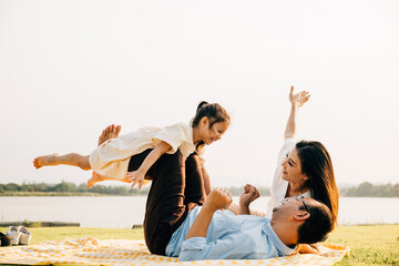 A joyful family moment in the park. Father holds his daughter up high as she smiles and flies like...