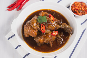 Ayam Sambal Balado or spicy fried chicken served on a plate on a white wooden table.