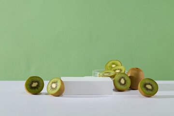 Pastel green background features a petri dish of kiwi slices placed behind an empty podium. Product...