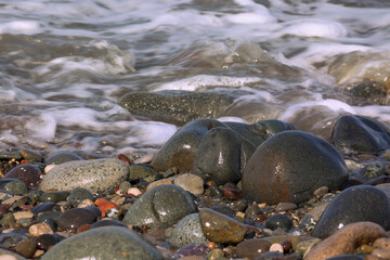 A wave runs over wet pebbles. The water's edge. Close-up