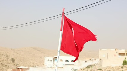 Tunisian flag is installed at highest point of impregnable fortress. Battered canvas of flag of Islamic country of Tunisia develops against background of blue sky