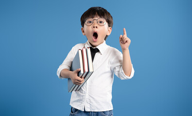 Portrait of an Asian school boy holding books and posing on a blue background