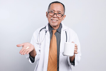 Senior Doctor Male Showing Medicine Pill While Holding Mug Isolated On White Background